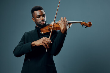 African American man in black suit playing violin in elegant musical performance on gray background