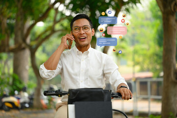 Happy male worker having phone call sitting on his bike at city park