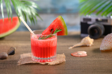 Glass of fresh watermelon juice on wooden table with seashells and camera. Summer drink concept