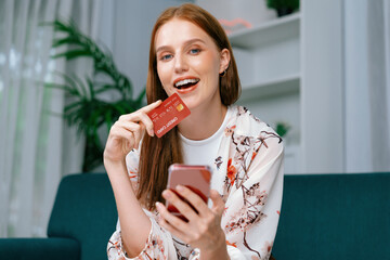 Young happy woman buy product by online shopping at home while ordering items from the internet with credit card online payment system protected by utmost cyber security from online store platform - obrazy, fototapety, plakaty