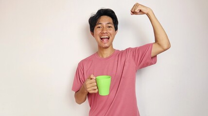 young asian man happy and excited posing raising both hands and cheerful and holding a cup on...