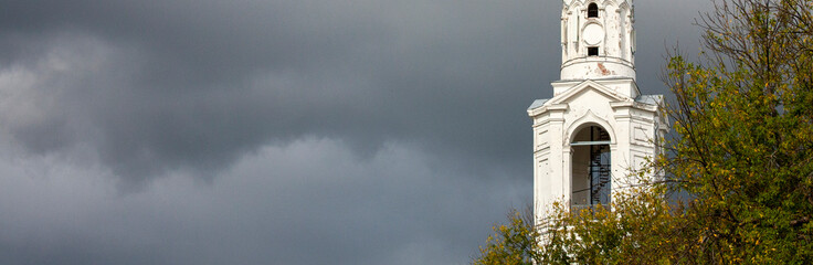 View of the snow-white bell tower with a gilded dome against the background of the autumn sky in...