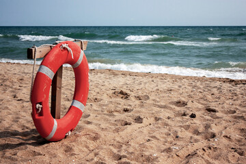 Red lifebuoy on the shore of a sandy beach on a sunny day. Lifebuoy and sea in summer.