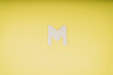 Letter M in wood on yellow background