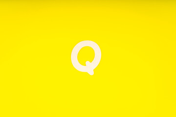 Letter Q in wood on yellow background