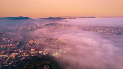 Misty morning reveals urban structures and natural beauty. Sunrise paints the sky in soft hues....