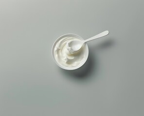 Top view of a white spoon in a plastic bowl with Greek yogurt isolated on a gray background in a closeup