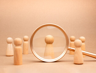Human resource (HR), hiring, selection, recruitment, CRM, right people and unique concepts. Wooden figure human, the chosen one person from crowd in magnifier lens on beige background.