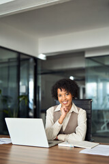 Confident happy young female lawyer, smiling professional African American business woman company manager executive working on laptop in office sitting at desk looking at camera, vertical portrait.