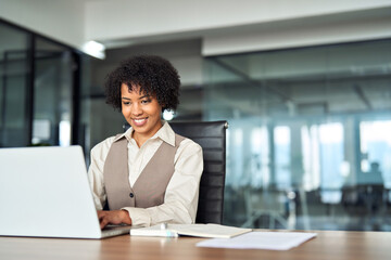 Professional happy business woman employee working on computer in office. Young smiling busy African American female company manager using laptop managing financial project sitting at desk. Copy space