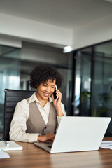 Young happy African American professional business woman executive making call having conversation at work. Female manager or entrepreneur talking on the phone using laptop at office desk. Vertical