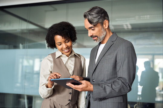 Two busy happy diverse professional business team people working in office with digital tablet. Male executive manager talking to female partners having conversation standing at work using tab.