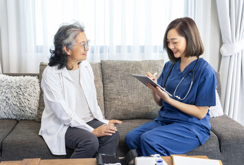 young asian female nurse in uniform visiting a senior patient at home,evaluate,collect data and provide advice patient care by using tablet,concept of aging care,home care,home health care