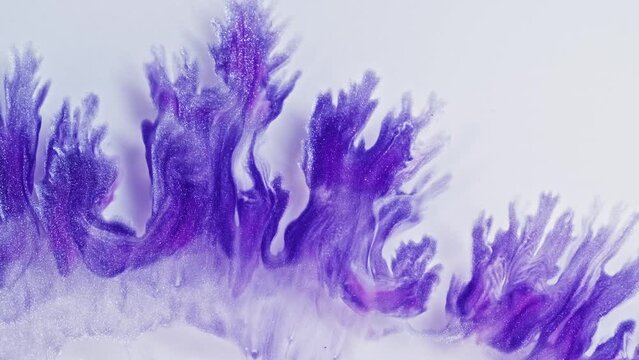 Purple and pink swirls in an acrylic pour painting create intricate patterns on a white background. The fluidity of the liquid paint creates delicate lines that resemble fractal structures.