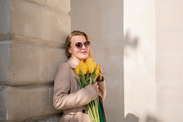 Woman holding yellow tulips, leaning against stone wall. Women's holiday concept, giving flowers.