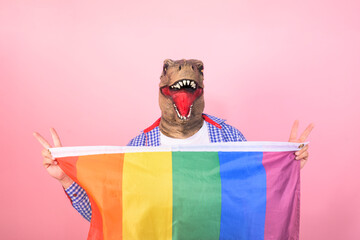non-binary person with a dinosaur head showing a rainbow flag while making the symbol of peace love