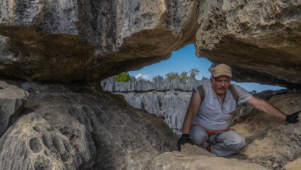 A tired man with a backpack and safety equipment crouched in the opening of the rocks, leaning on...