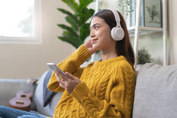 Relax at home on holidays concept,  Young Asian female wearing headphone and listening music in the living room.