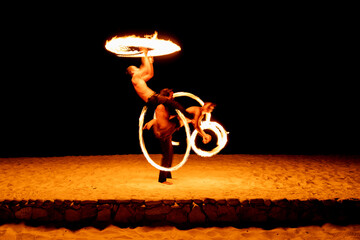 Silhouetted performers with flaming poi creating a stunning visual effect on the shore