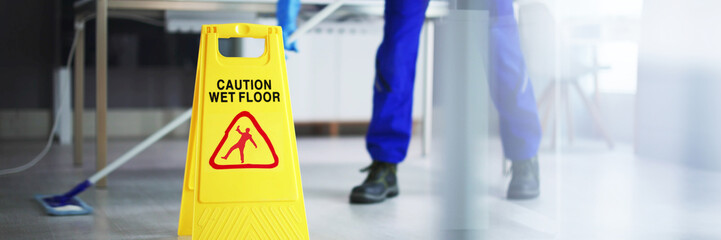 Male Janitor Cleaning Floor With Caution Wet Floor Sign