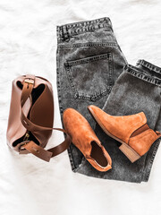 Women's grey mom jeans, brown leather tote bag, suede chelsea boots on a light background, top view
