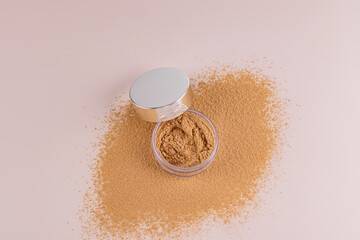 Top view of an open jar with loose powder of beige, bronze tone stands on a scattered sample of powder. A copy of the space. Make up.