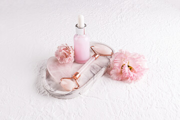 Rose quartz roller massager, gua sha scraper, massage and care oil in a matte bottle on white ceramic tray. Top view. Lifting effect.