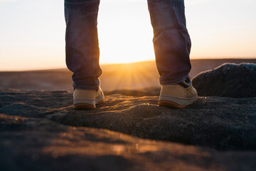 closeup of feet of man in  boots reaching destination and on top of mountain at sunrise or sunset....