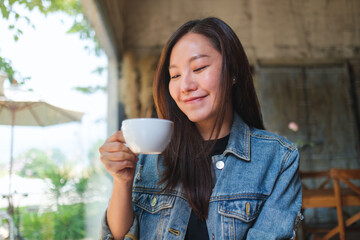 Portrait image of a beautiful young asian woman holding and drinking hot coffee in cafe - 797410164