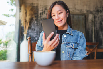 Portrait image of a young woman holding and using mobile phone in cafe - 797410386