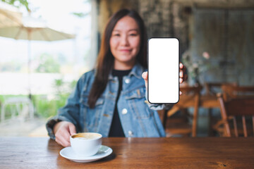 Mockup image of a woman showing a mobile phone with blank white screen in cafe - 797410792
