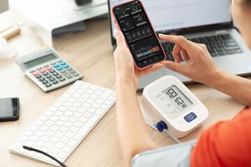 Woman working at computer desk checking on smartphone different health care apps display