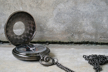 A black pocket watch with a chain on a gray stone surface.