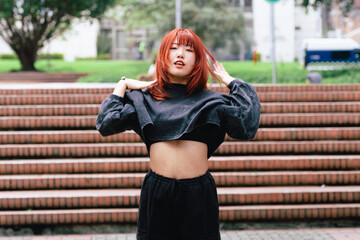 Red-haired Korean woman expressing exuberance through dance in an urban space