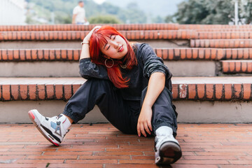 Korean woman with red hair seated on steps, in a reflective pose