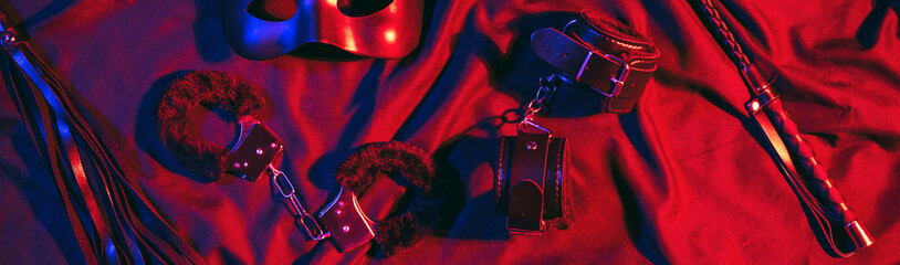 set of BDSM sex toys with handcuffs, a whip flogger for submission and domination on a red...
