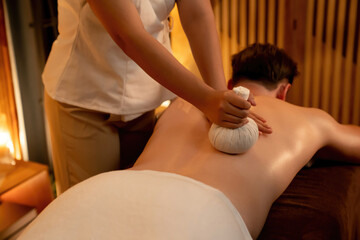 Hot herbal ball spa massage body treatment, masseur gently compresses herb bag on man body....