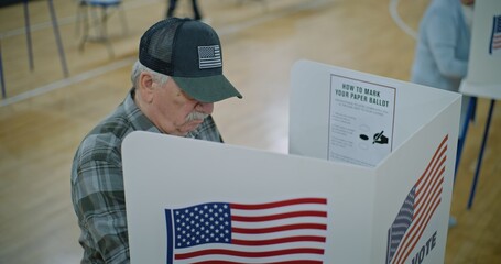 Elderly male voter with bulletin in hands comes to voting booth. American citizens come to vote in...