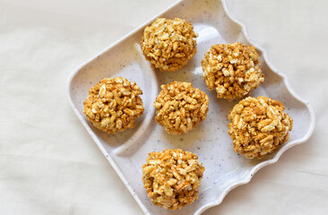Bengali Traditional Puffed Rice Balls is a sweet made using puffed rice mixed with jaggery, Murmura Laddoo, Churmura Laddoo or Pori Urundai. flattened rice sweet ball or Chirar moa on white tray.
