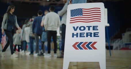 Vote here sign on the floor. Queue of multi ethnic American citizens come to vote in polling station. National Election Day in United States. Political races of US presidential candidates. Civic duty.
