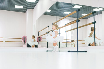 Portrait of a cute baby ballerina sitting near the ballet barre putting on shoes