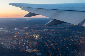 View from an airplane of the city and its surroundings. Beautiful evening aerial landscape. Buildings and streets under the wing of an airplane. Flying on an airplane. Travel and aviation tourism.