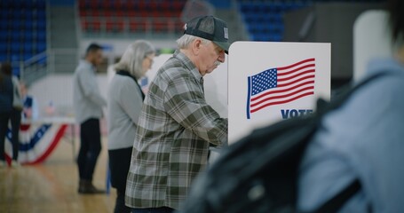 Male voter with bulletin in hands comes to voting booth. American citizens come to vote in polling station. Political races of US presidential candidates. National Election Day in the United States.