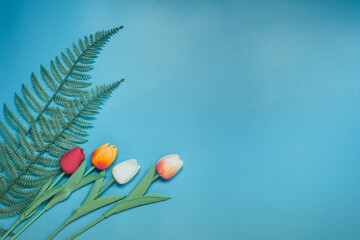 minimal flat lay summer time concept with fern tropical leaf and  tulip on pastel blue background...