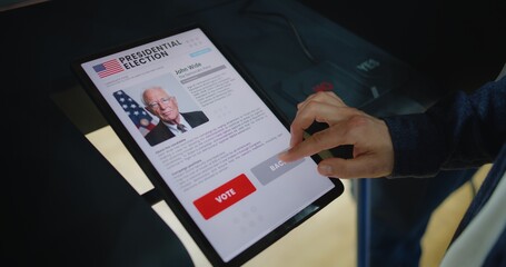 Close up of Caucasian man making choice and voting for US presidential candidate in voting booth using tablet computer. US citizen at polling station during National Election Day in the United States.