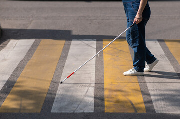 Close-up of the legs of a blind woman crossing the road at a crosswalk with a cane. 