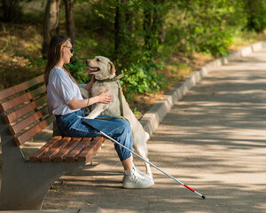 Blind young woman cuddling with guide dog while sitting on a bench. 