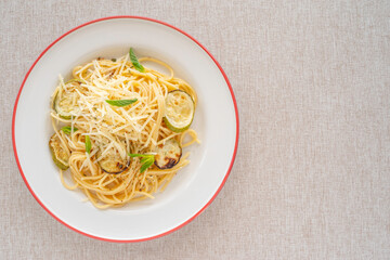 Spaghetti with grilled zucchini, parmesan cheese, spices on ceramic plate over cotton fabric background.