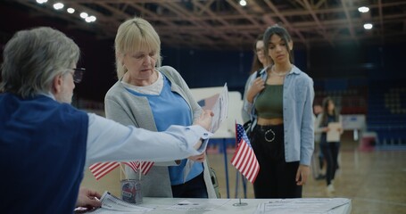 American citizen comes to vote in polling station, take bulletins. Mature polling officer consults voters. Political races of US presidential candidates. National Election Day. Civic duty. Dolly shot.