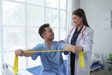 Obraz premium Physical therapist gives resistance band exercises. About the arms and shoulders of male office workers, office syndrome, male patient. Physiotherapy concept.